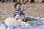 A child sitting on a blue and white patterned blanket with a  collection of sea life themed cuddly animals from Senger placed in front of them.