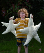 A child holding up a small and large Senger starfish soft toys in front of them. The Senger starfish are part of a wide range of organic soft toys available here at babipur. 