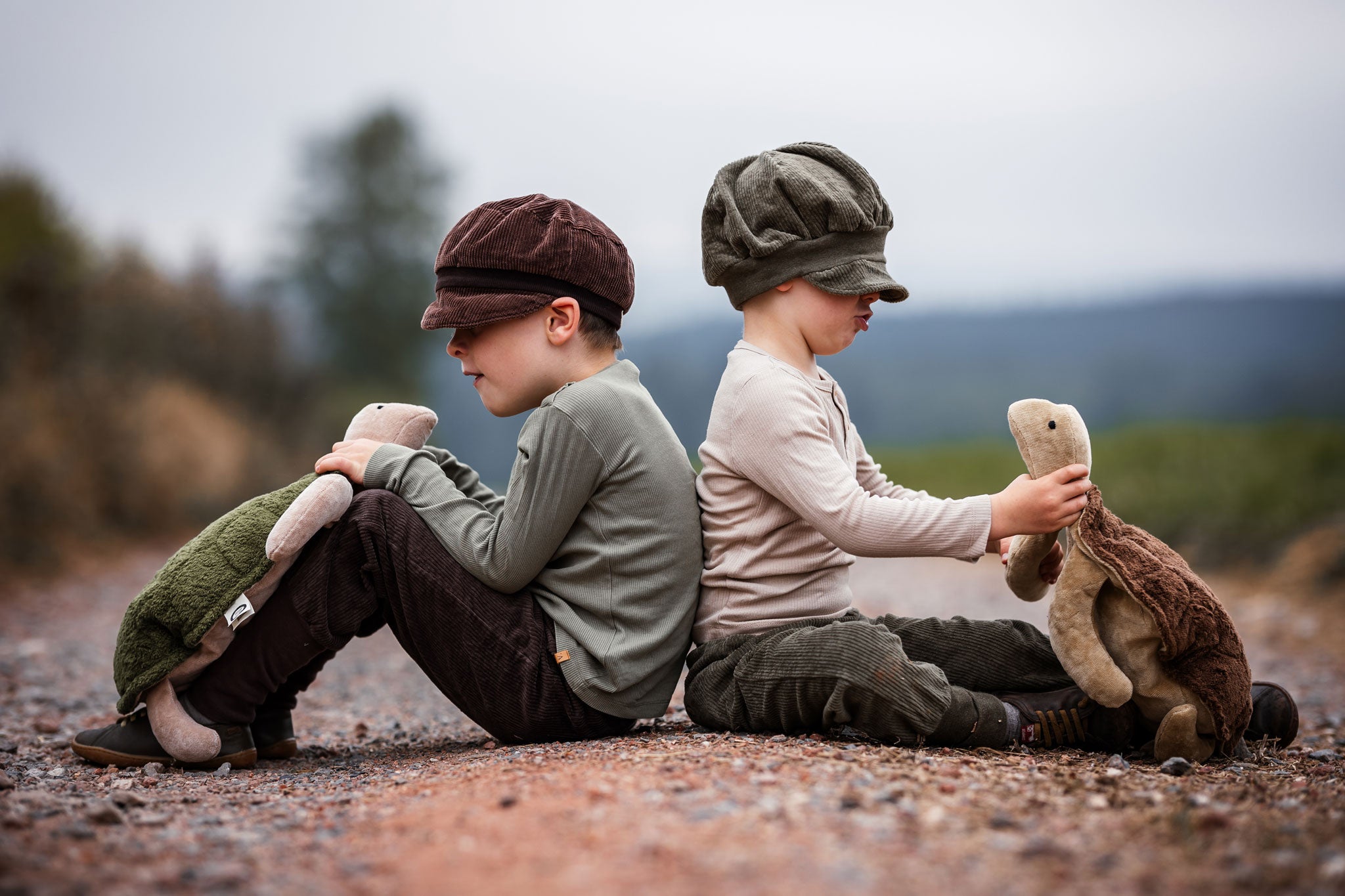 Two children sitting on the ground facing away from each other, each child is holding a large Senger turtle in their hands.