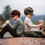 Two children sitting on the ground facing away from each other, each child is holding a large Senger turtle in their hands.