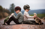Two children sitting on the ground facing away from each other, each child is holding a large Senger turtle in their hands.