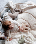 A child lying on a soft blanket and playing with the beige Senger elephant grasper available at Babipur.