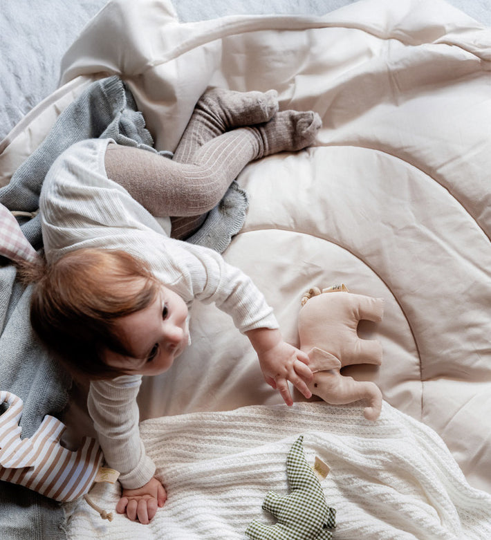 A child lying on a soft blanket and playing with the beige Senger elephant grasper available at Babipur.