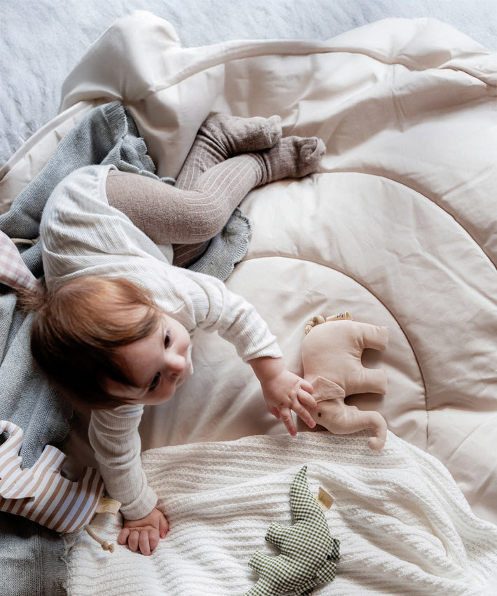 A child lying on a soft blanket and playing with the beige Senger elephant grasper available at Babipur.