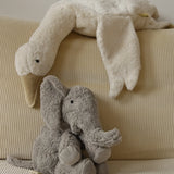A large Senger elephant cuddly toy with a white goose soft toy lying above on a corduroy cushion