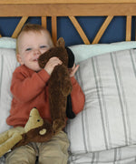 A child cuddling the Senger small floppy brown horse soft toy. There is a small floppy hedgehog soft toy resting on the child's knee.