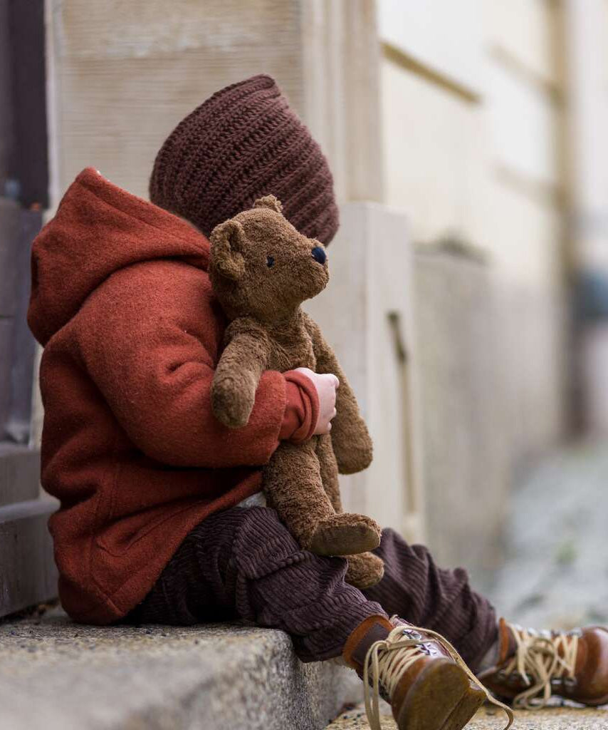 A toddler sat on a step, cuddling the Senger organic cotton loppy brown teddy bear