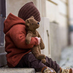 A toddler sat on a step, cuddling the Senger organic cotton loppy brown teddy bear