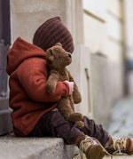A toddler sat on a step, cuddling the Senger organic cotton loppy brown teddy bear