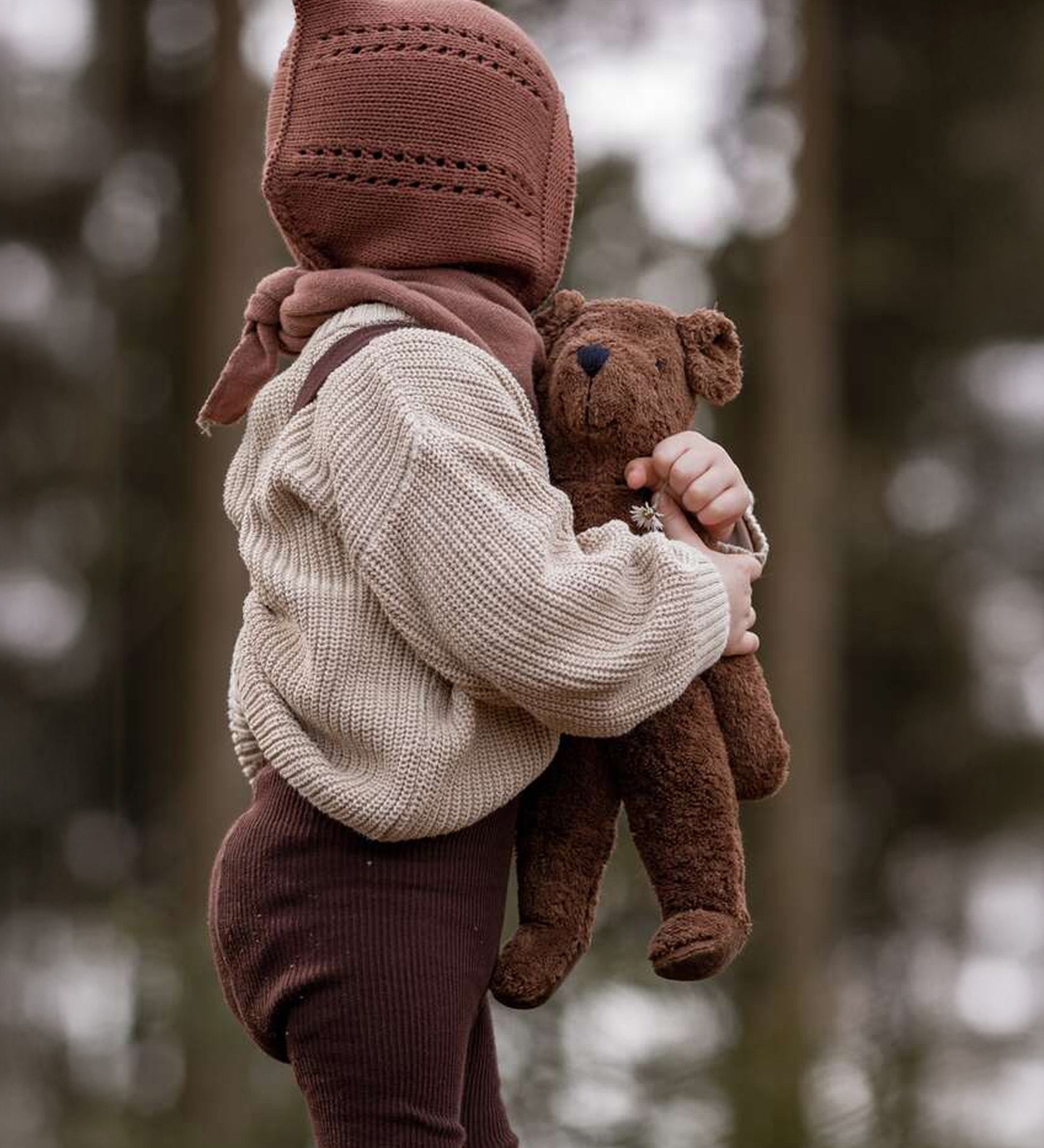 A toddler in the forest, holding the Senger organic cotton stuffed toy brown teddy bear