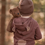 A toddler in the forest, holding the Senger organic cotton stuffed toy brown teddy bear