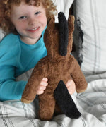 A child holding up the brown floppy horse soft toy from Senger showing the back of the animal. The horse has a brown body and a black mane and tail.