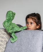 Child with a hand in a Senger GOTS organic cotton green frog puppet standing behind a sofa
