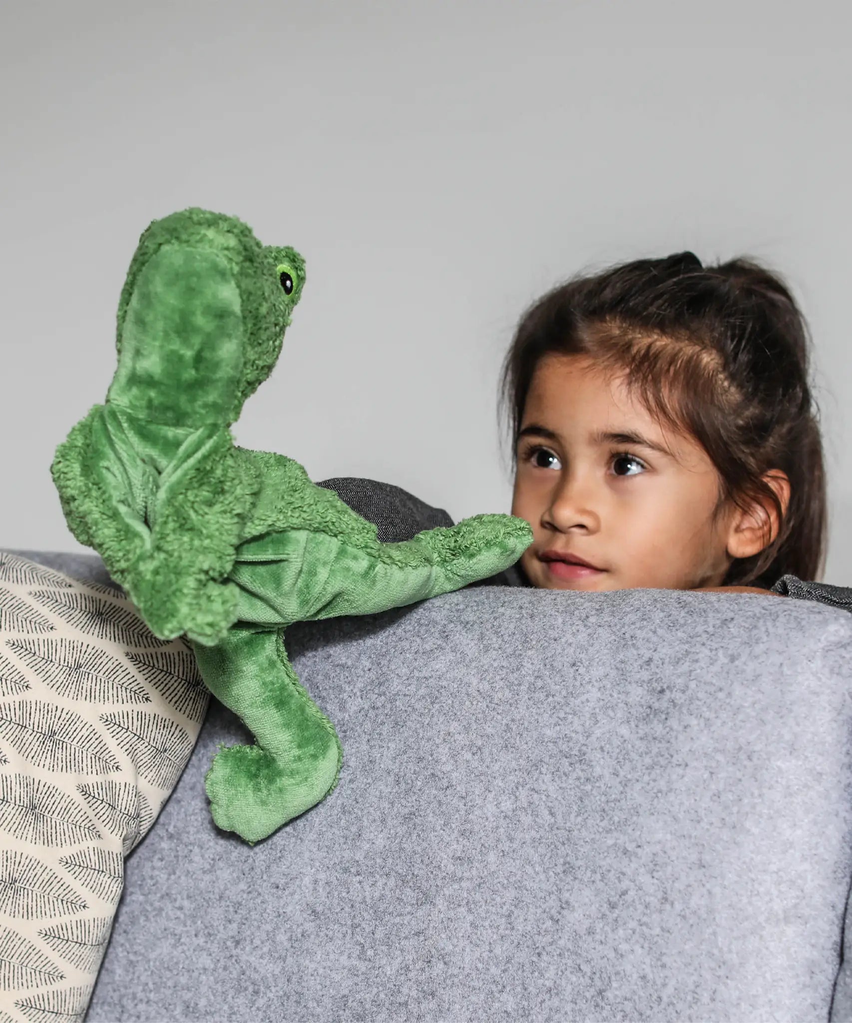 Child with a hand in a Senger GOTS organic cotton green frog puppet standing behind a sofa