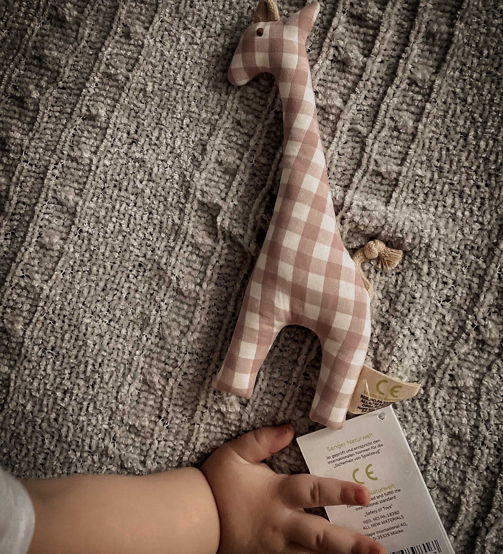 A baby's hand next to a Senger giraffe grasping toy available at Babipur showing scale of the grasping toy