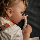A child with the Senger pink and white check giraffe soft grasping toy in hand, available at Babipur.