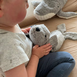 Child holding a small Senger grey seal cuddly toy by the head on a blanket
