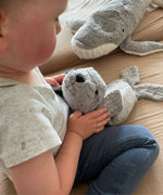 Child holding a small Senger grey seal cuddly toy by the head on a blanket