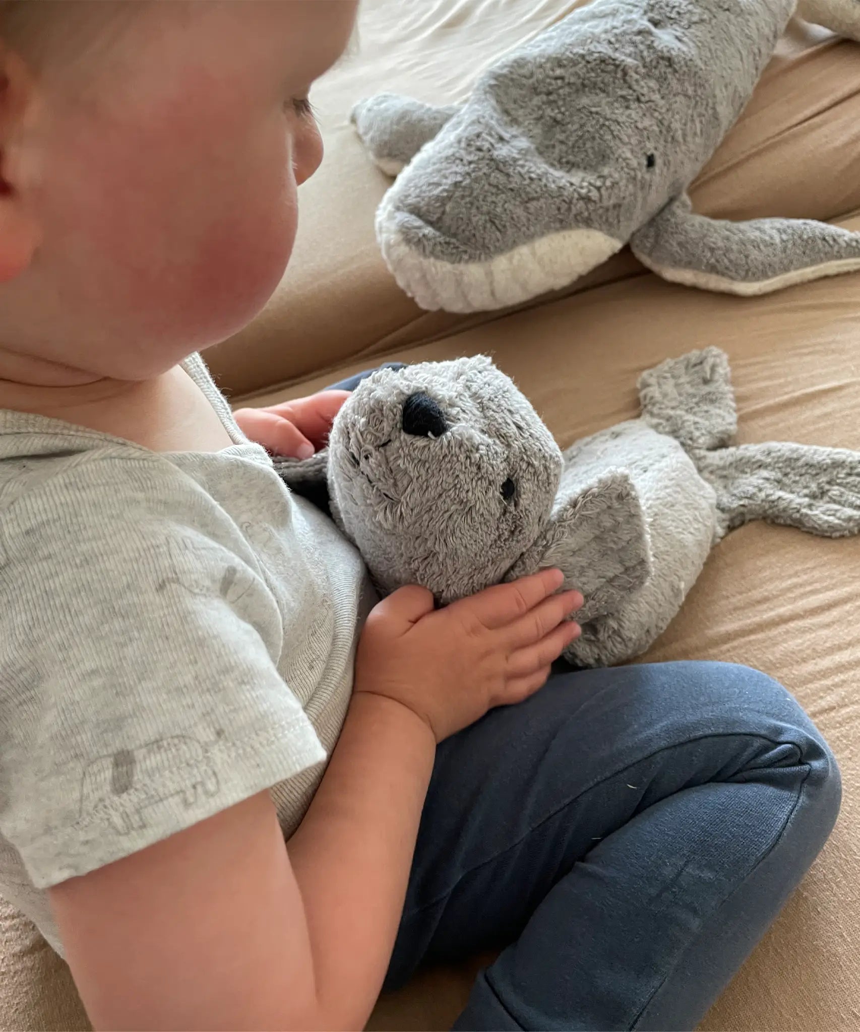 Child holding a small Senger grey seal cuddly toy by the head on a blanket