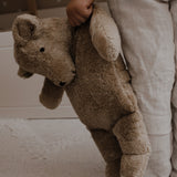 A large Senger cuddly bear being led in a child's hand by it's shoulder.