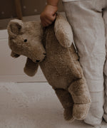 A large Senger cuddly bear being led in a child's hand by it's shoulder.