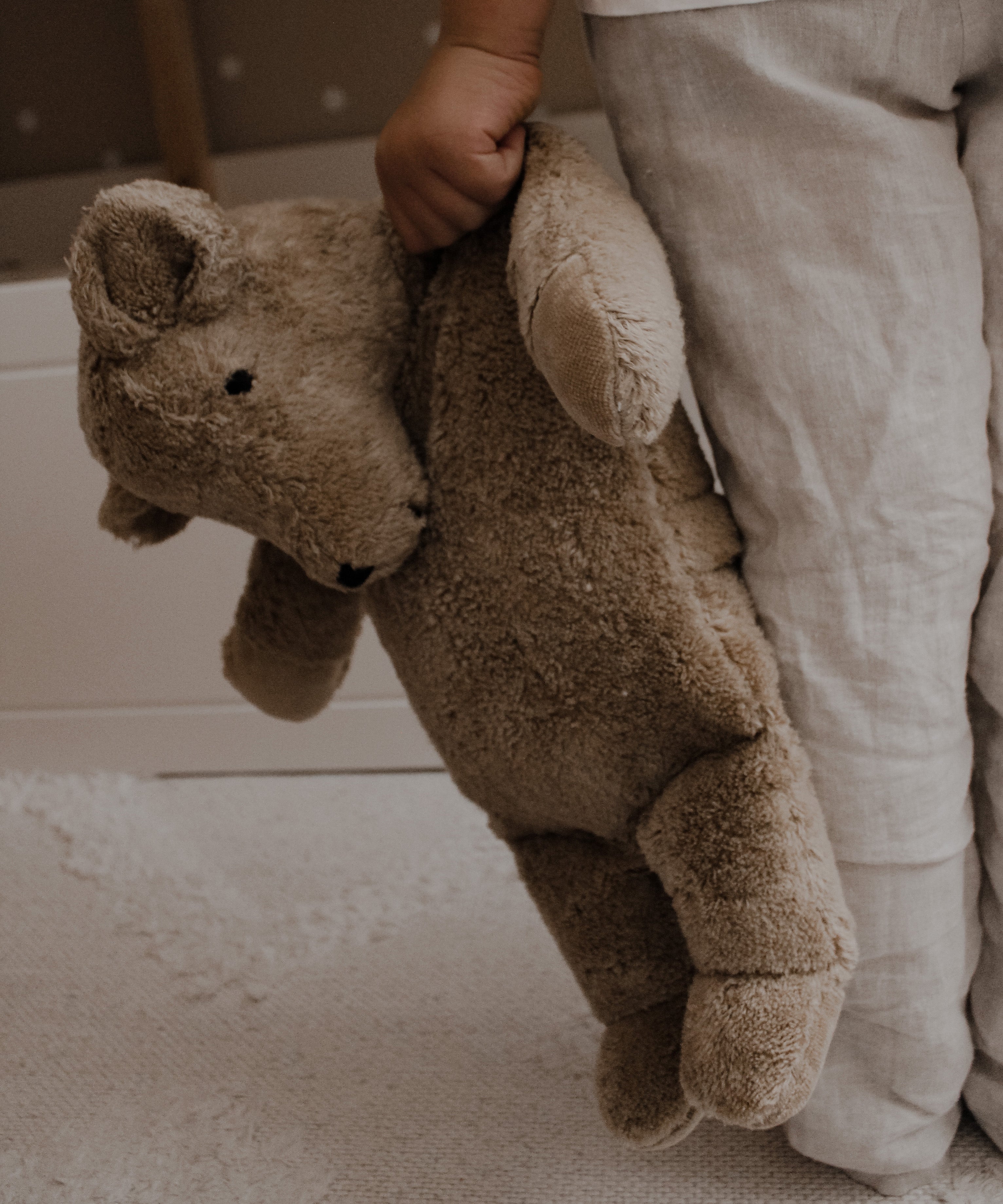 A large Senger cuddly bear being led in a child's hand by it's shoulder.