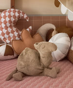 A large Senger camel cuddly soft toy standing on a blanket with cushions in the background