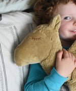A close up of the face of the large Senger Cuddly Camel Organic Heatable Soft Toy. The camel is being cuddled by a child. The large camel soft toy is part of a wide selection of soft toys made from organic cotton and natural fillings available at Babipur.