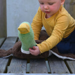 A child sitting on wooden plank holding up the Senger Large Cuddly Drake Duck soft toy's neck.