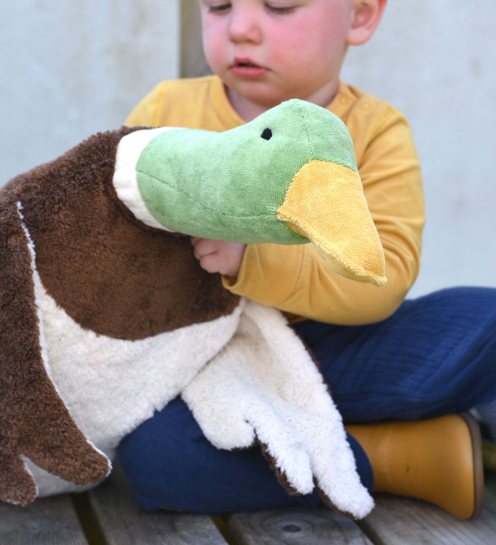A close up of the Senger Large Cuddly Drake Duck soft toy in a child's hands.