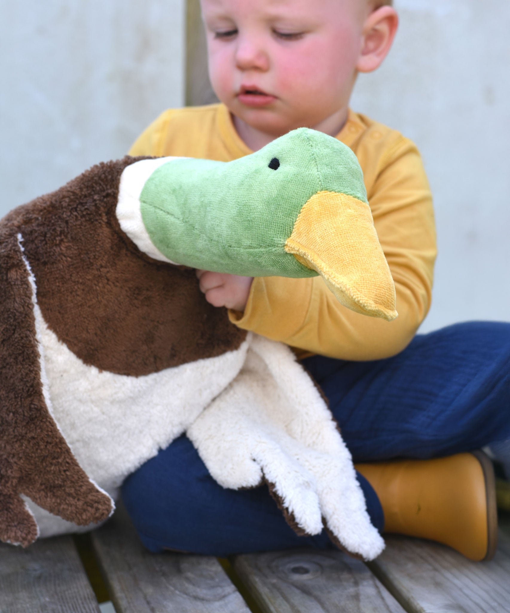 A close up of the Senger Large Cuddly Drake Duck soft toy in a child's hands.