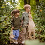Two children holding hands walking in a forest, one is holding a Senger Large Cuddly Goose organic soft toy in a creamy Linen colour. The other child has the smaller version of the goose. These soft toys are created from the highest quality, sustainable and traceable natural materials. Senger cuddly animal toys and soft dolls are handmade in Germany with love and attention to detail and we are proud Senger stockists here at Babipur. 