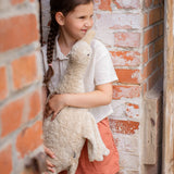 Child holding a large cream Senger cuddly goose soft toy outdoors standing against a brick wall