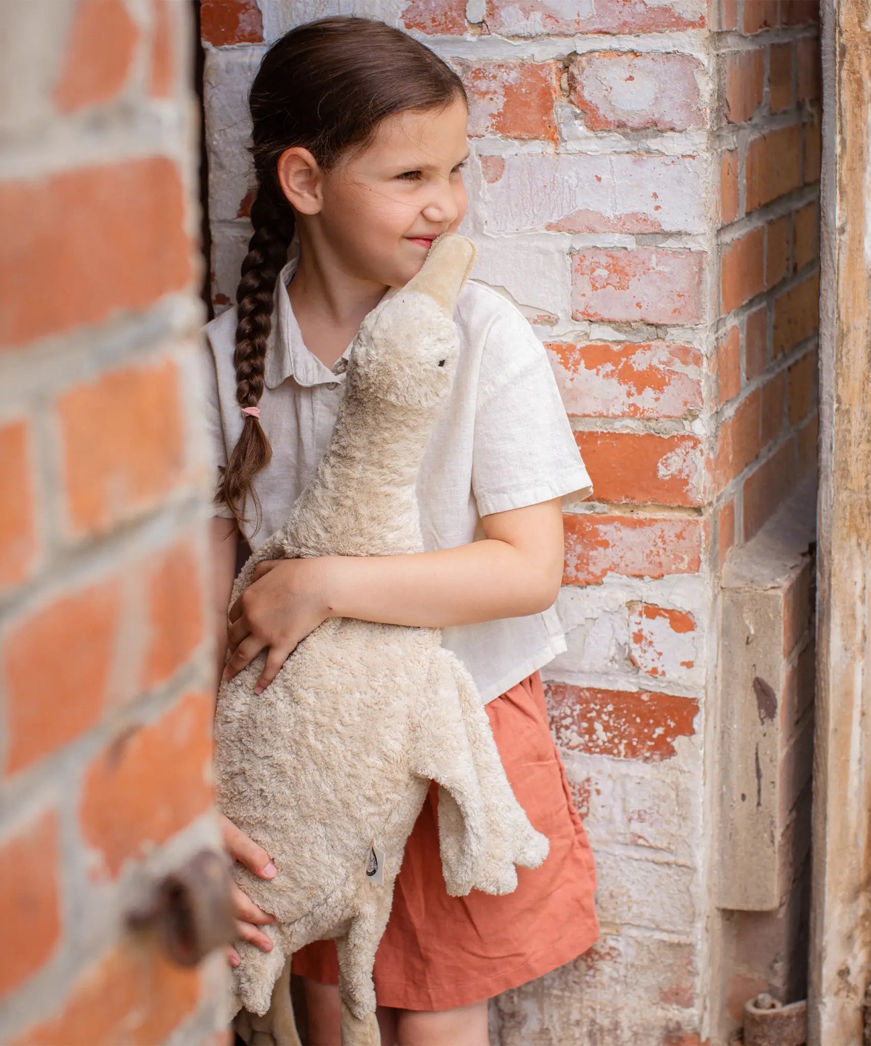 Child holding a large cream Senger cuddly goose soft toy outdoors standing against a brick wall