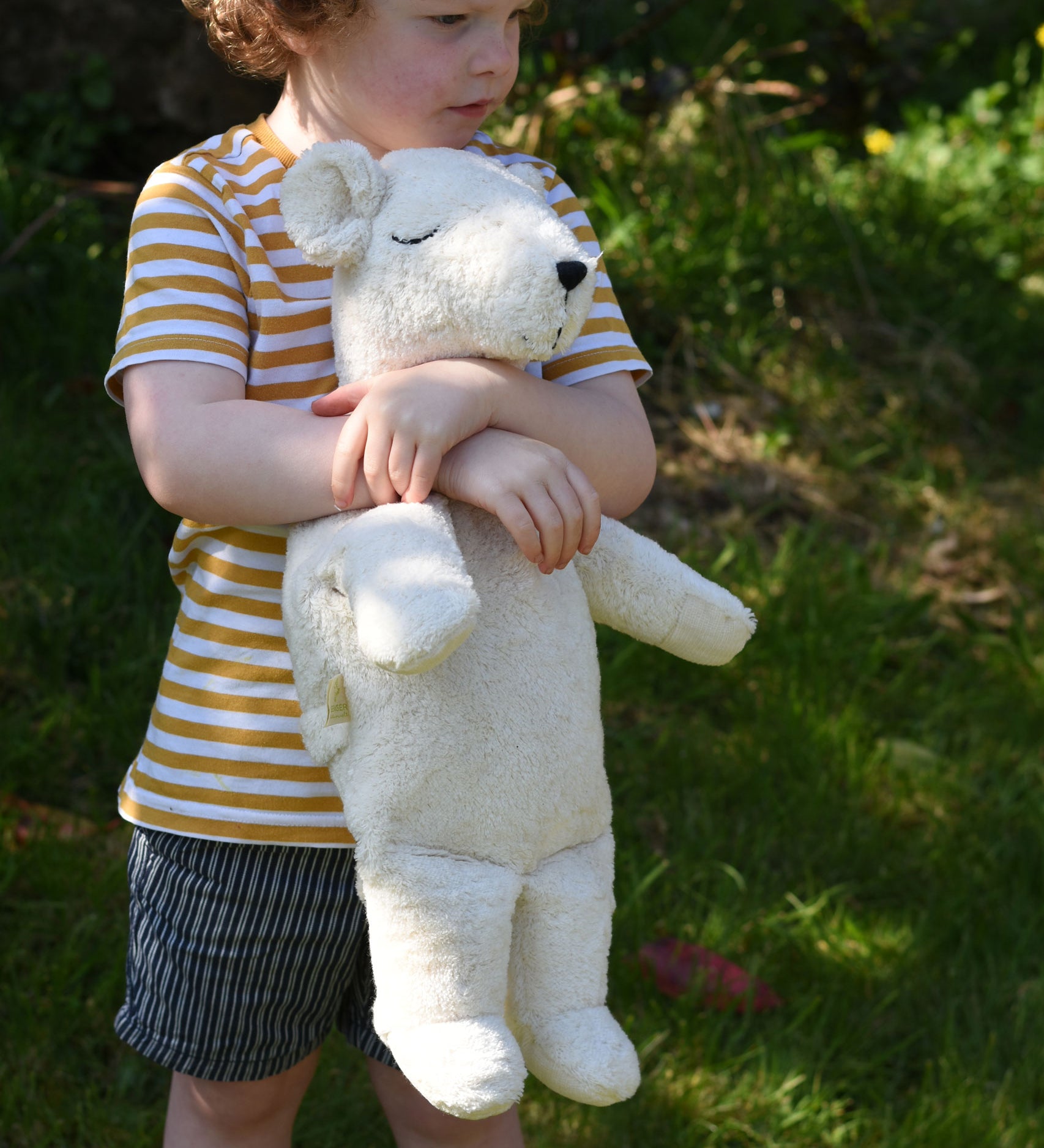 A child cuddling the Senger large cuddly polar bear soft toy in their arms.