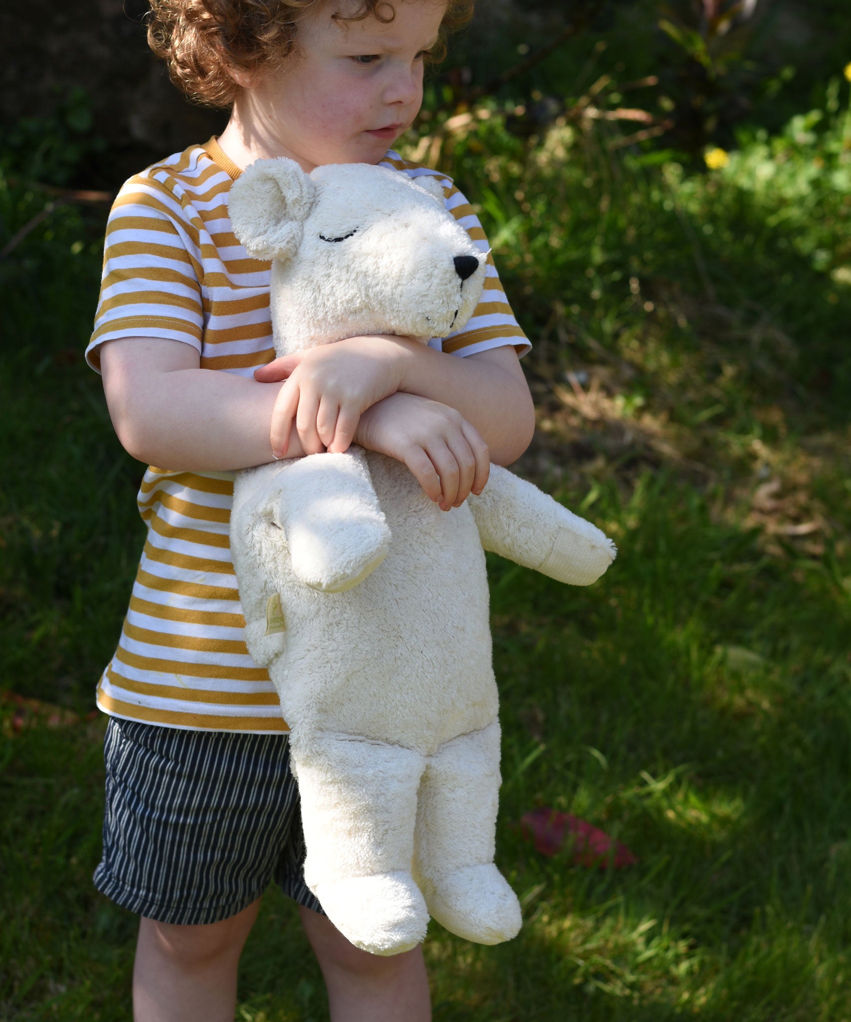 A child cuddling the Senger large cuddly polar bear soft toy in their arms.
