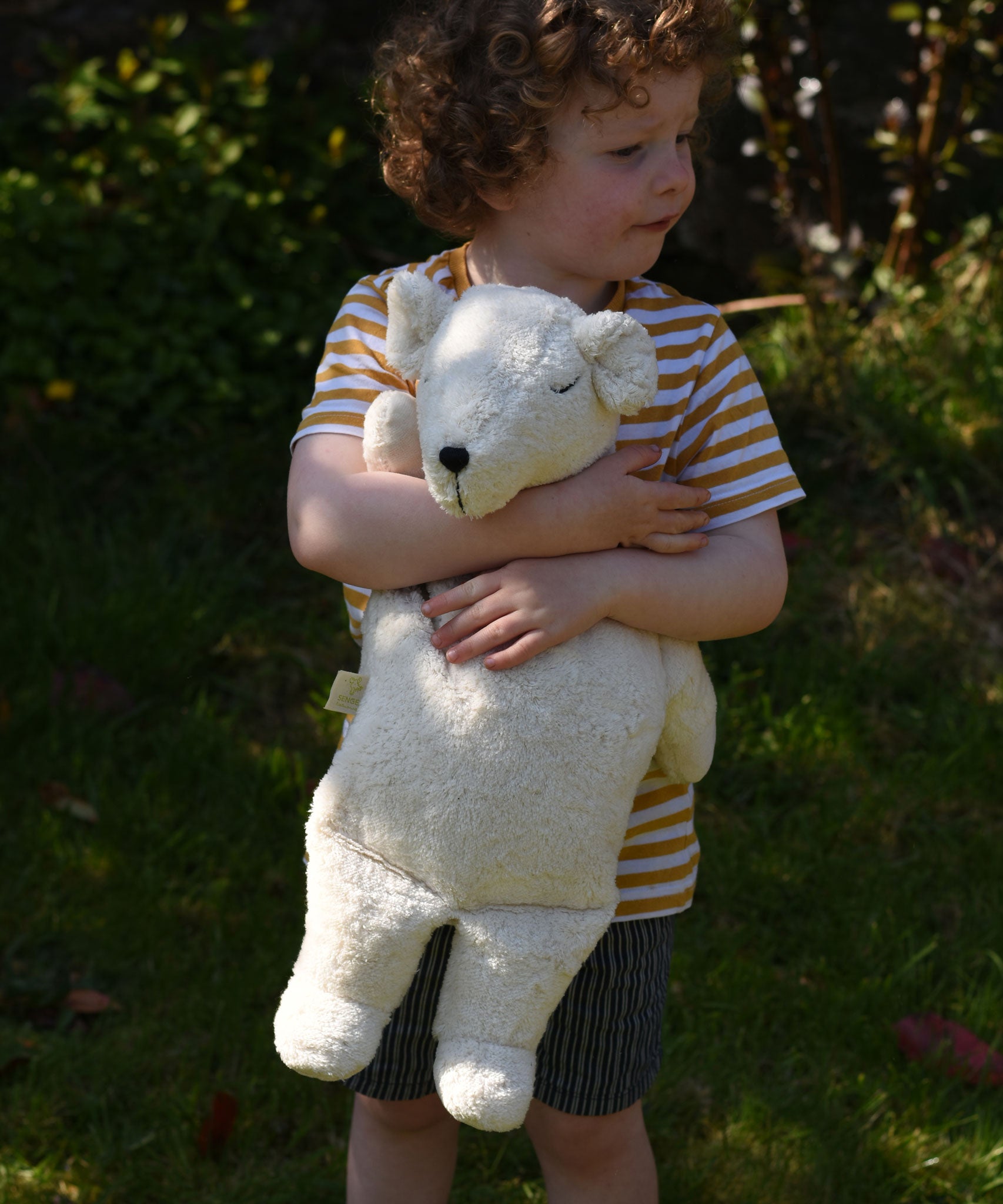 A child cuddling the Senger large cuddly polar bear soft toy in their arms.
