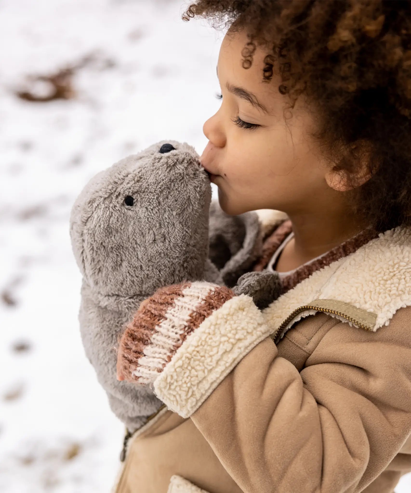 Child holding and kissing a large Senger grey cuddly soft toy in the snow
