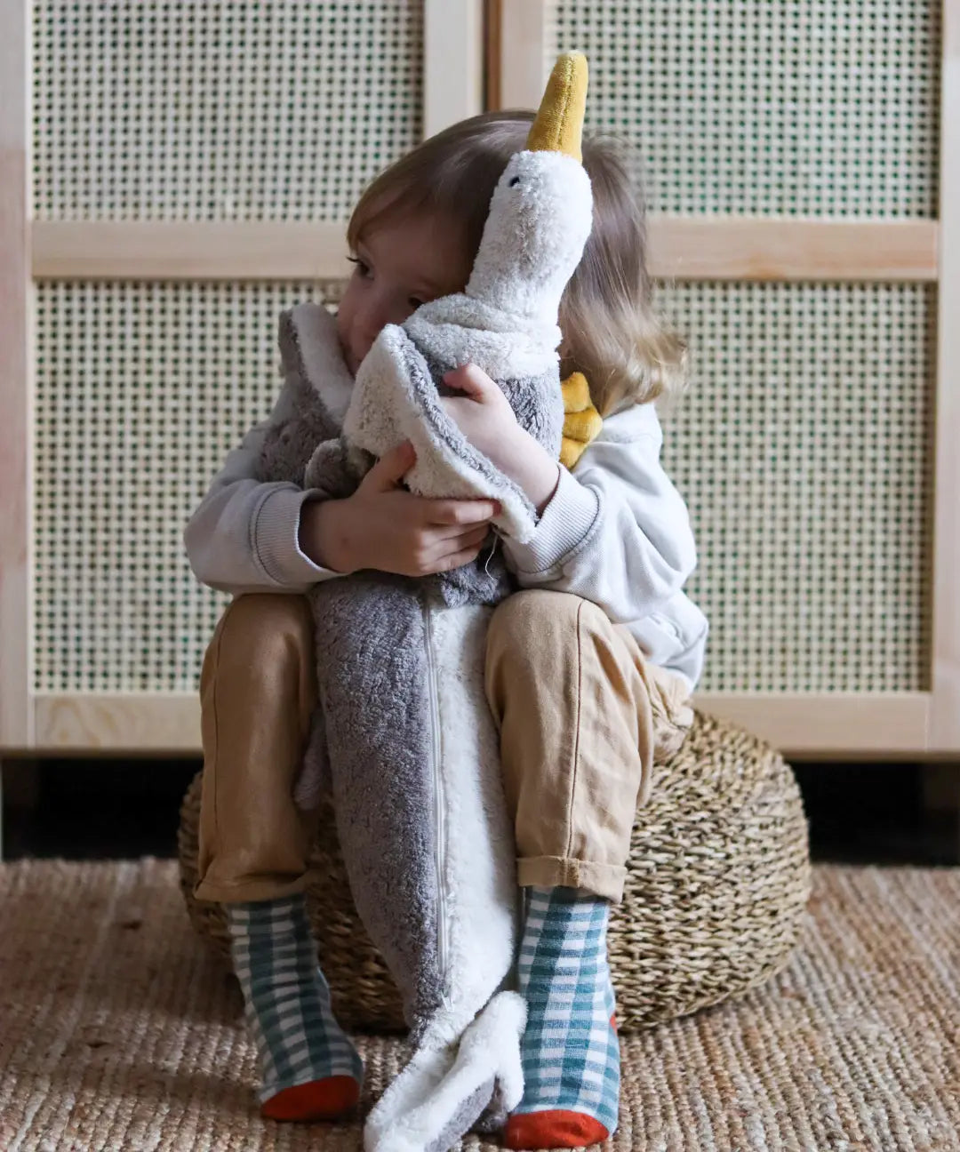 Child hugging a large Senger dolphin and seagul cuddly toys and sitting on a woven cushion
