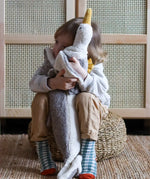 Child hugging a large Senger dolphin and seagul cuddly toys and sitting on a woven cushion