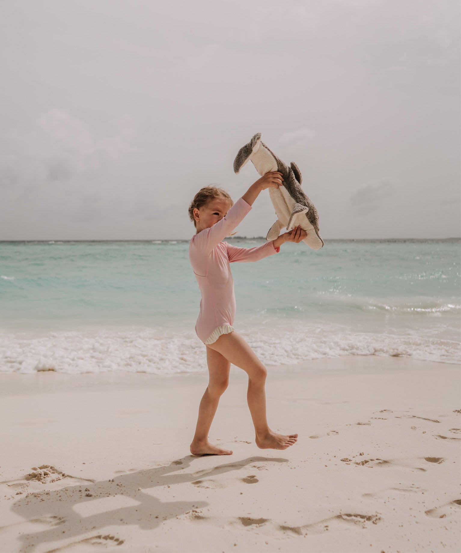A little girl playing with the Senger large organic cotton stuffed dolphin toy on the beach