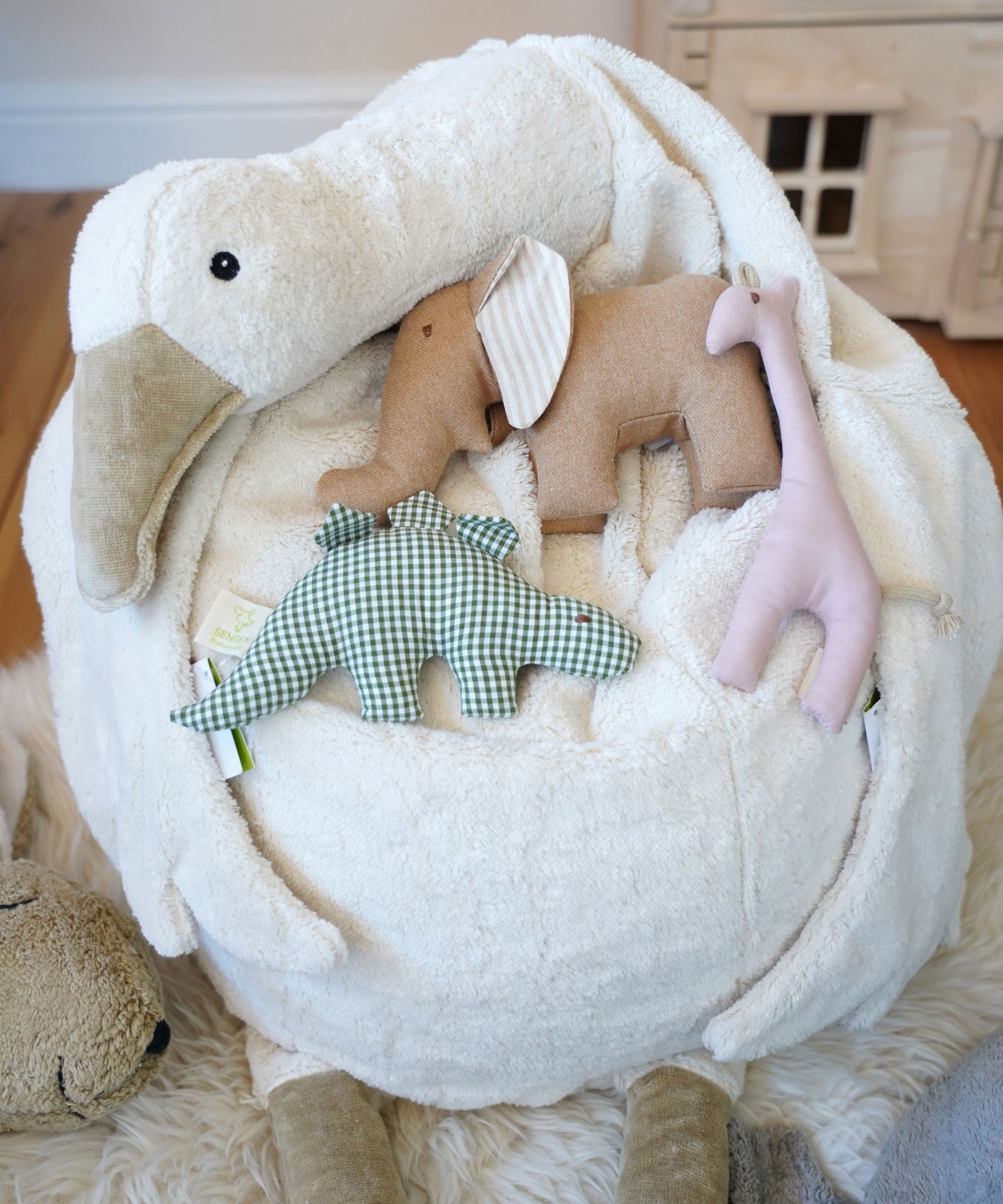 A close up of a Senger Goose bean bag shown with smaller Senger animal baby clutching toys placed on it.