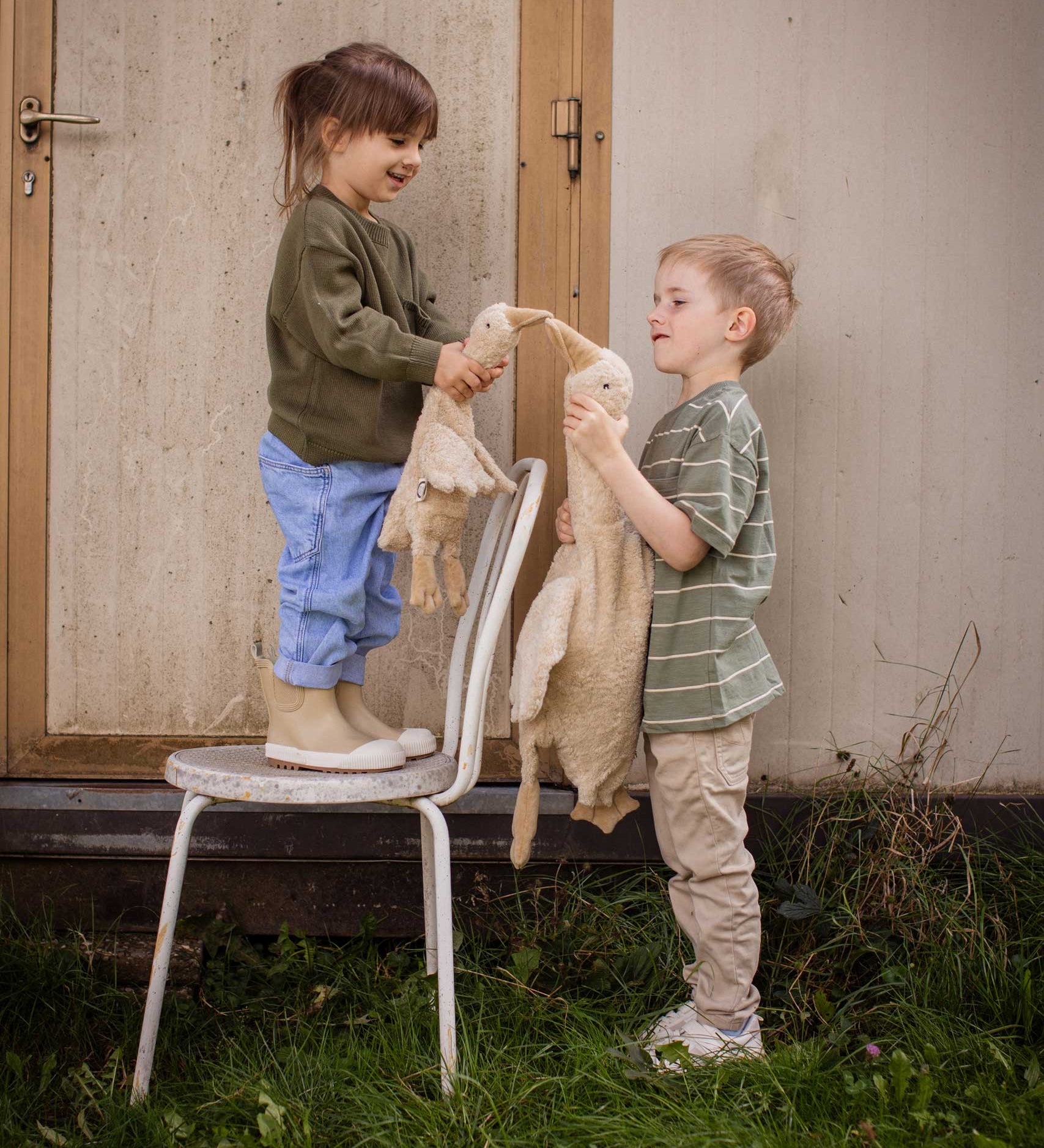 Two children holding a Senger Cuddly Goose organic soft toy in a creamy Linen colour. One is standing on a chair and holding a small goose the other is ho;ding a large goose. These soft toys are created from the highest quality, sustainable and traceable natural materials. Senger cuddly animal toys and soft dolls are handmade in Germany with love and attention to detail and we are proud Senger stockists here at Babipur. 
