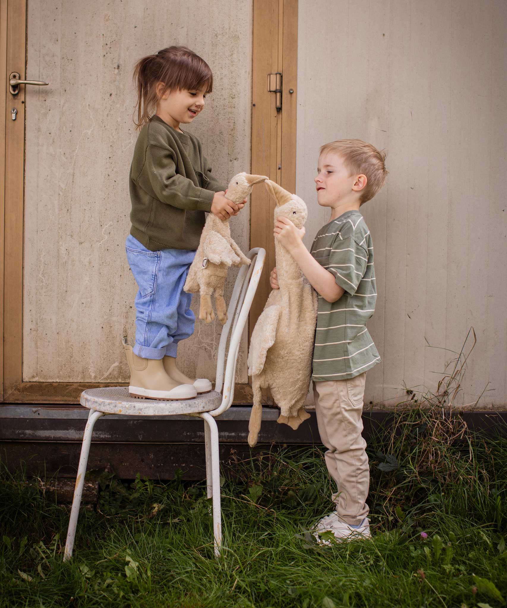Two children holding a Senger Cuddly Goose organic soft toy in a creamy Linen colour. One is standing on a chair and holding a small goose the other is ho;ding a large goose. These soft toys are created from the highest quality, sustainable and traceable natural materials. Senger cuddly animal toys and soft dolls are handmade in Germany with love and attention to detail and we are proud Senger stockists here at Babipur. 