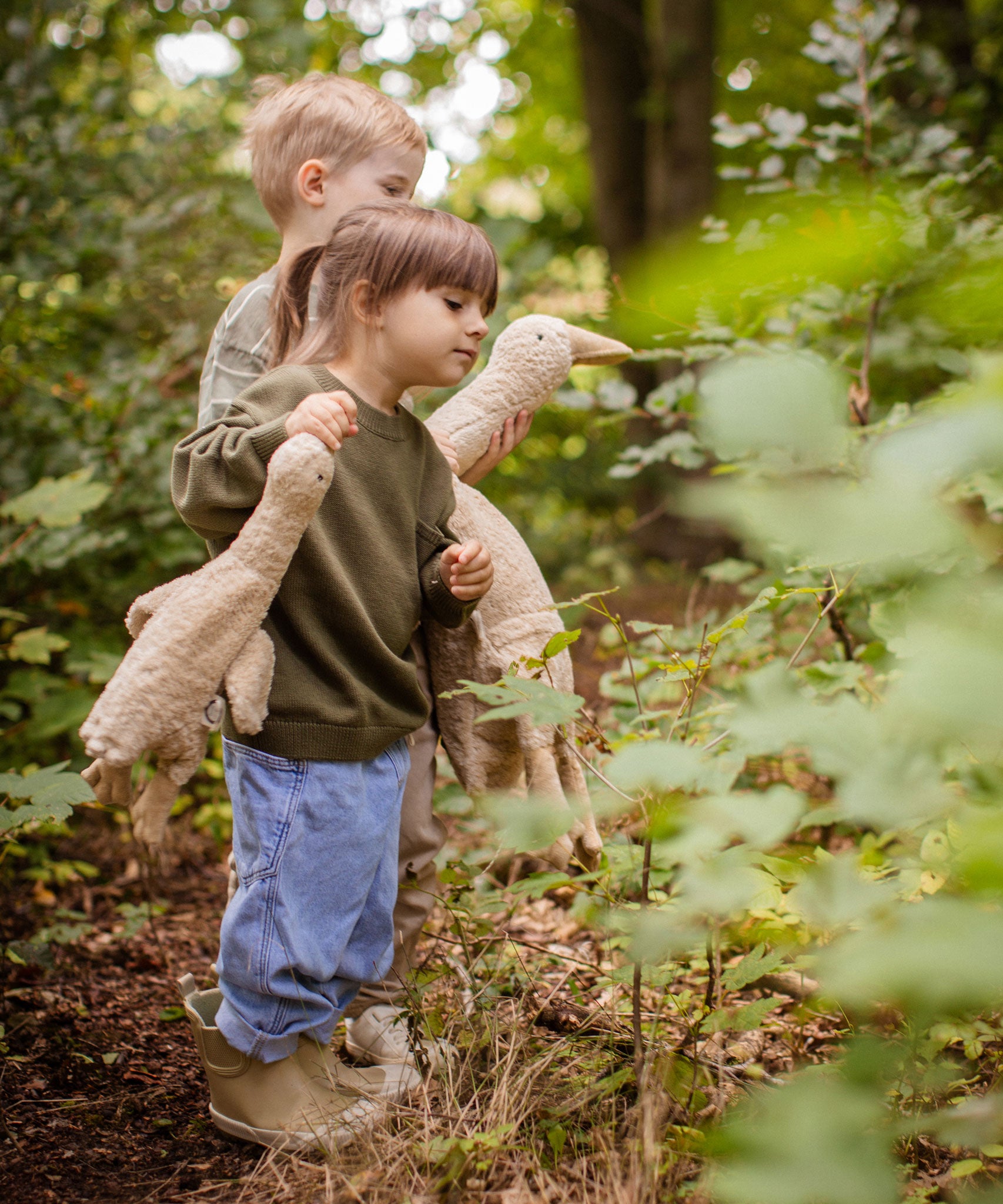 Two children walking in a forest, one is holding a Senger Large Cuddly Goose organic soft toy in a creamy Linen colour. The other child has the smaller version of the goose. These soft toys are created from the highest quality, sustainable and traceable natural materials. Senger cuddly animal toys and soft dolls are handmade in Germany with love and attention to detail and we are proud Senger stockists here at Babipur. 