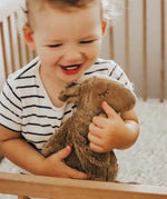 A toddler in a cot, cuddling the Senger small organic cotton stuffed camel toy