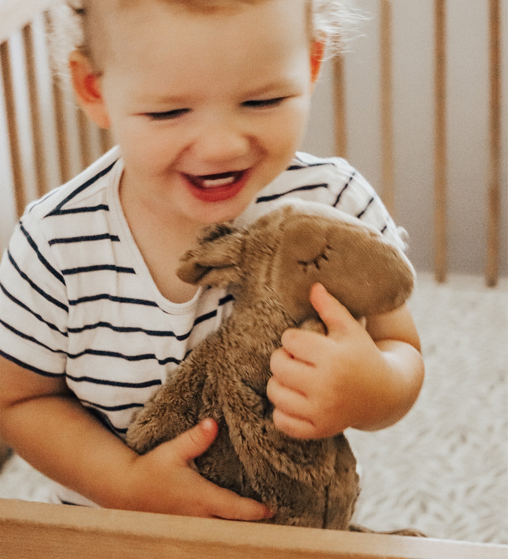 A toddler in a cot, cuddling the Senger small organic cotton stuffed camel toy