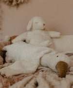 A Senger large white cuddly goose soft toy lying flat on a blanket with a sheep soft toy in the background