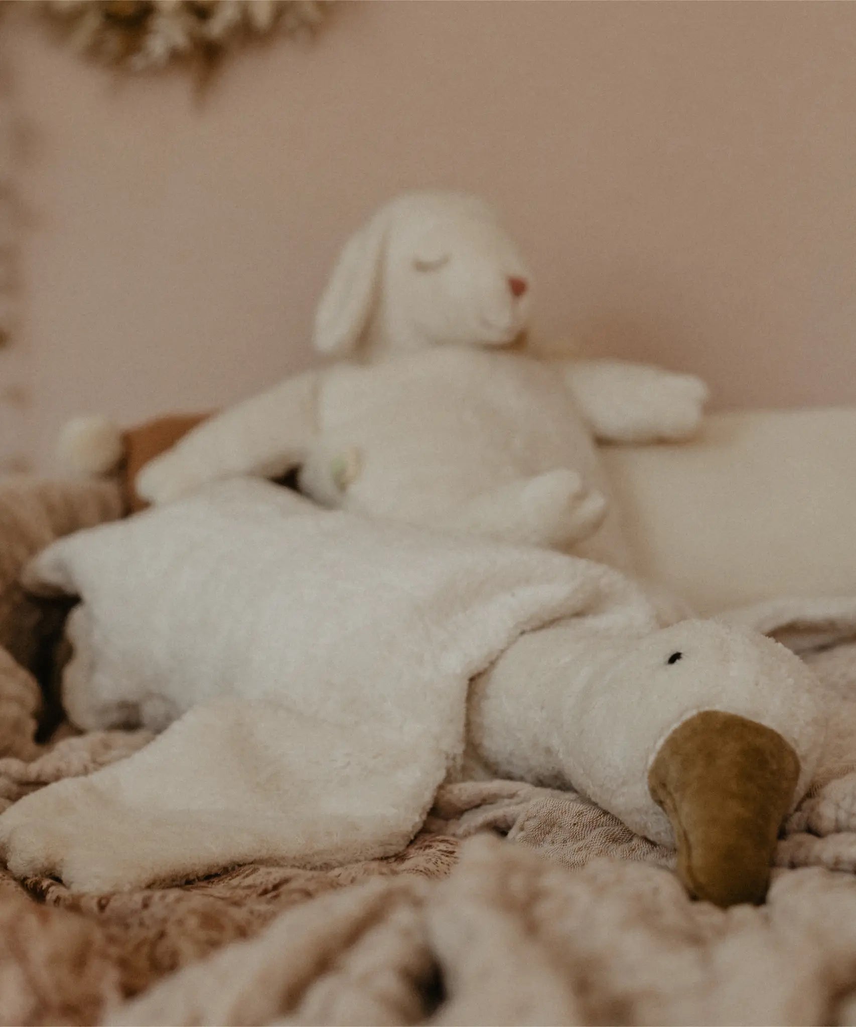 A Senger large white cuddly goose soft toy lying flat on a blanket with a sheep soft toy in the background