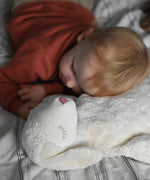 A young child laying down with his head resting on a Senger large white sheep cuddly soft toy. This cuddly sheep is made with organic cotton and natural fillings. This sheep is part of a wide range of soft toys stocked at Babipur. 